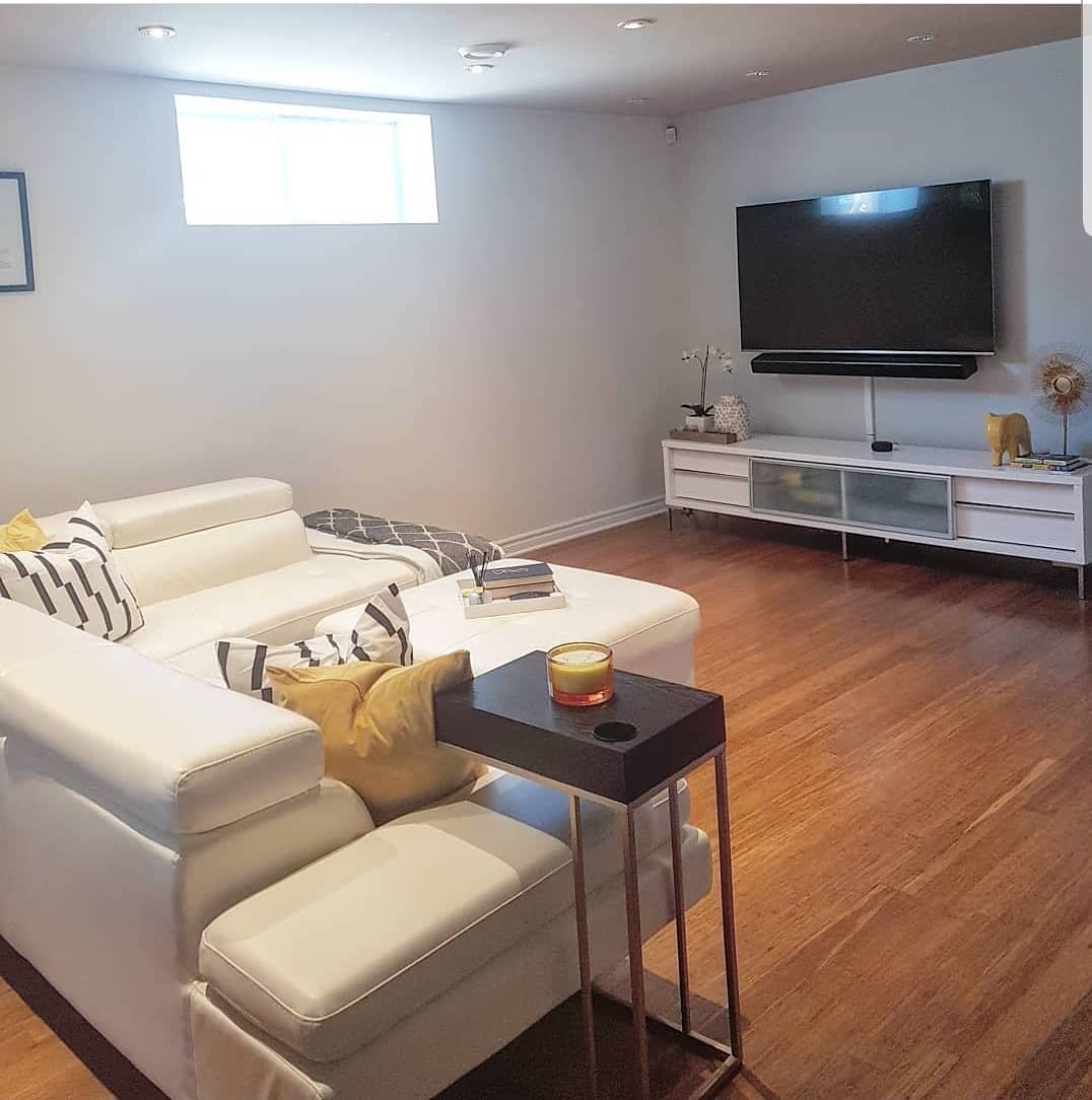 Modern basement living room with white sectional, wall-mounted TV, and wooden floors.